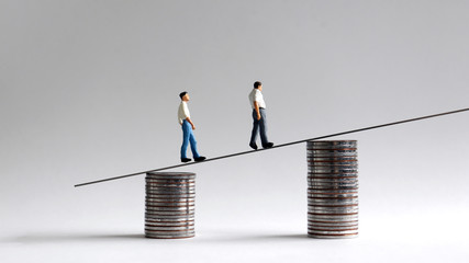 Two miniature men walking on two piles of coins.