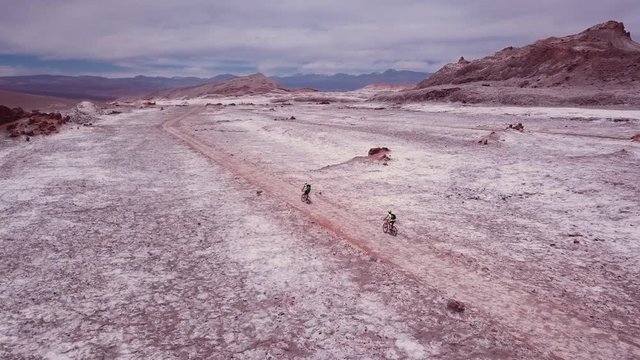 Bicycle travelers exploring the  desert road in the salt flats of Atacama. Aerial view, 4k.