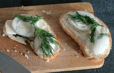 Closeup two sandwiches with bread, butter, eggs and dill on wooden board in black background. Making a sandwiches.