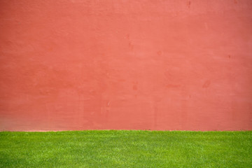 Solid color copy space background plaster paint wall in red pink color with fresh green grass lawn foreground on sunshine day