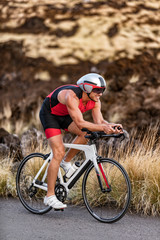 Triathlon professional cyclist man cycling road racing bike in time trial helmet and compression tri suit in Hawaii landscape for Kailua-Kona ironman. Triathlete biking in nature.