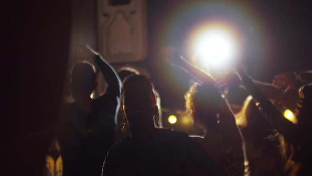 Medium shot of unrecognizable young people swaying hands to rhythmic music when partying in nightclub