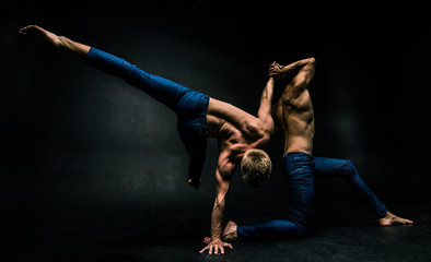 Male acrobatic duo performs a complicated balancing act on a dark background