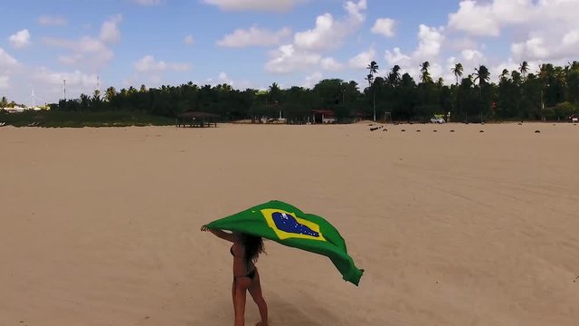 Aerial image of beautiful girl holding the flag of Brazil.