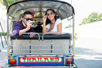 Young couple tourists traveling on local Tuk Tuk taxi in Bangkok, Thailand