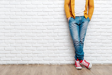 Young fashion man's legs in jeans and sneakers on wooden floor