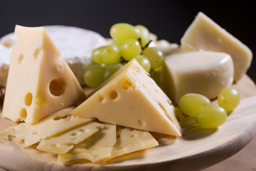 Different kinds of cheese on a plate with grapes and nuts