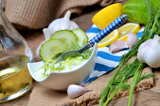 Close-up Of Spoon In Tzatziki - Traditional Greek Dressing Or Dip Sauce, Garlic, Lemon, Dill, Cucumber, Jug With Oil And Decoration In Background