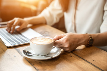 Close up the hand of an Asian girl is freelancer woman, she is working by using the laptop computer and driking a cup of coffee on morning in a coffee shop or her office.