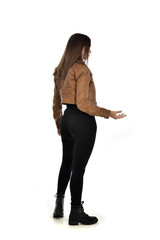 full length portrait of brunette girl wearing brown leather jacket.   standing pose with back to...
