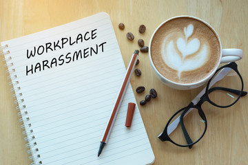 Workplace harassment concept on notebook with glasses, pencil and coffee cup on wooden table. Business concept.