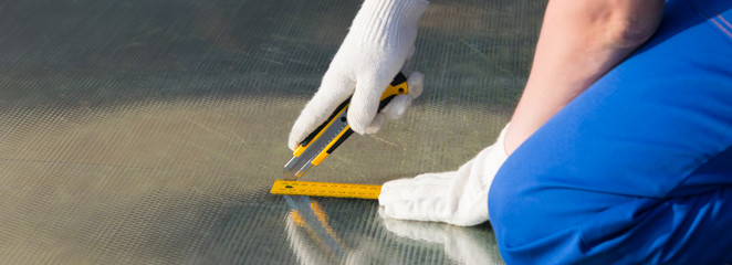 man in gloves, cuts polycarbonate with a knife on the yellow ruler there is a place for the...