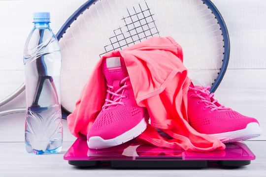pink sneakers and a T-shirt, for fitness, on an electronic scales, a bottle of water, on a gray background and tennis rackets