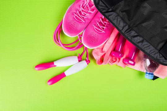 pink clothes and accessories for fitness, a bottle of water, in a sports bag, on a light green background