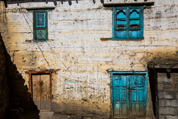 Fototapeta na wymiar Image of traditional nepalese house facade at Annapurna circuit trek in Jhong village in Mustang region in Nepal. Bright turquoise windows