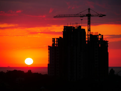 Industrial building site at sunset with crane on an office or apartment block under construction silhouetted against a colorful red  sky. Construction site at sunset.