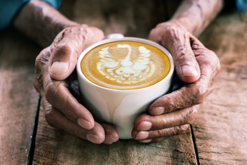  Hands of old man holding cup of coffee on the wood table.vintage tone