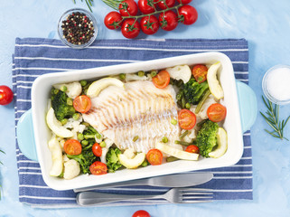 Fish cod baked in blue oven with vegetables - broccoli, tomatoes. Healthy diet food. Blue stone background, top view.