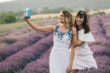 Two woman having fun with soap bubbles at flower field
