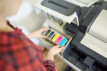 From above shot of anonymous woman putting set of ink into plotter in printing office. 