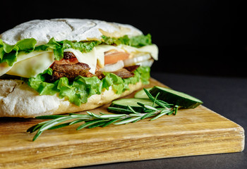 big sandwich on black background rosemary cucumber wooden board Street food, fast food. Homemade burgers with beef, cheese  on the wooden table. Toned image.