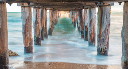 Misty waves underneath of a pier during sunset