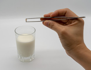 Handing holding milk teeth and little root with tweezer over a glass of milk