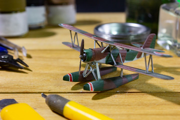 Plastic model WW2 biplane with scale model tools on wooden workbench closeup.