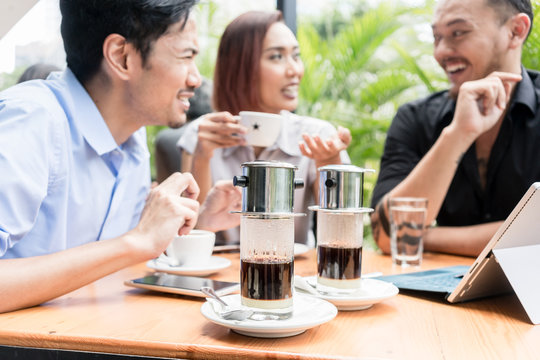 Delicious Vietnamese coffee served on the table of three young cheerful Asian friends outdoors in a modern cafeteria