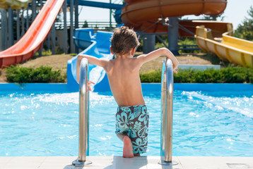 healthy small boy in shorts standing near summer blue swimming pool in water park