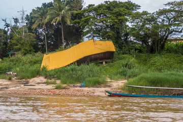 A collapsed house with a yellow painted metal roof on the riverside of the Tembeling river in...