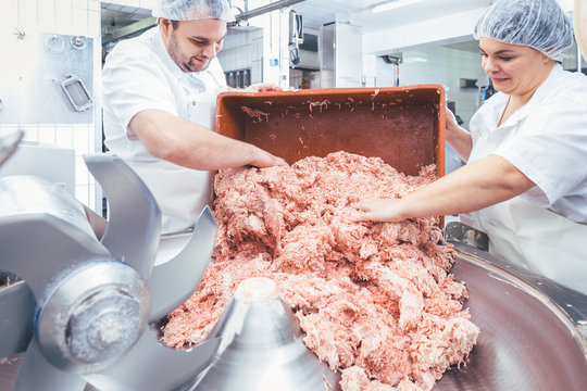 Team of butchers taking minded meat out of grinder machine for further use