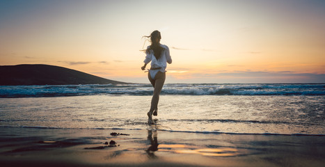 Woman at the beach in sunset running into the water