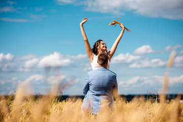 The groom holds his beautiful bride in the middle of a wheat field
