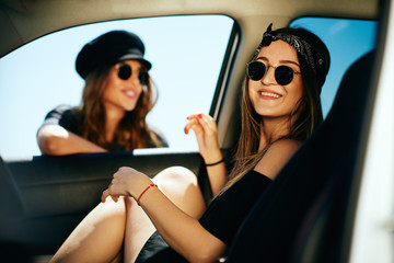 Two women taking a break from driving. One woman in the car and other leaning on the car window.