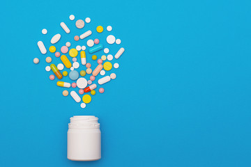 Assorted medical pills and capsules scattered from a bottle on a blue background. Empty place for...