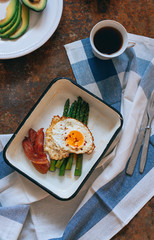 Flat lay breakfast with coffee, avocado, asparagus, egg and bacon, view from above on a rusty background