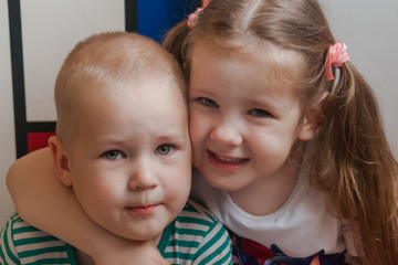 Family portrait close-up of two children. Sister hugs brother by the neck, shoulders