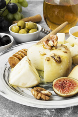 Snacks with wine - various types of cheeses, figs, nuts, honey, grapes on a gray background