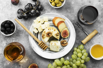 Snacks with wine - various types of cheeses, figs, nuts, honey, grapes on a gray background. Top view. Food background