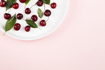 Ripe cherry and green leaves on a pink background. Top view, copy space. Food background