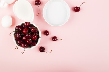 Ingredients for cherry pie - milk, eggs, cherry, sugar on a pink background. Top view, copy space. Food background
