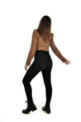 full length portrait of brunette girl wearing brown leather jacket.   standing pose with back to the camera on white background.