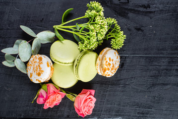 Sweet colored macaroons in composition with flowers on black background. Copy space