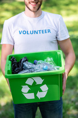 partial view of smiling volunteer holding recycling box with plastic waste