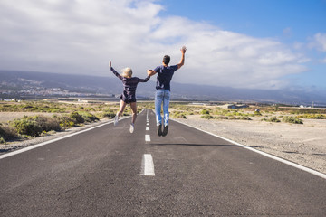 happiness concept for couple in love and friendhsip jump together in the middle of a long road. travel and life in relationship, wanderlust and beautiful world to explore. vacation time.