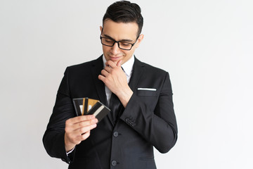 Thoughtful mixed race businessman looking at credit cards. Pensive handsome young male manager in glasses thinking of his profit and choosing credit card. Many opportunities for business concept