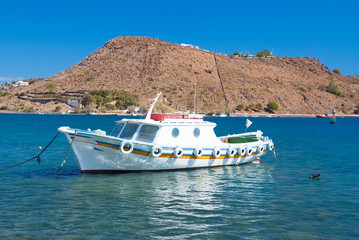 Fototapeta premium Summer vacation and sea travel. Boat in blue sea in Patmos, Greece. Small ship at seaside with mountain on sunny sky. Vessel and water transport. Wanderlust and discovery