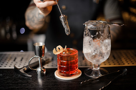 Bartender stirring a fresh red cocktail with a decorative spoon