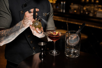 Professional bartender spraying on the red cocktail with a special liquid